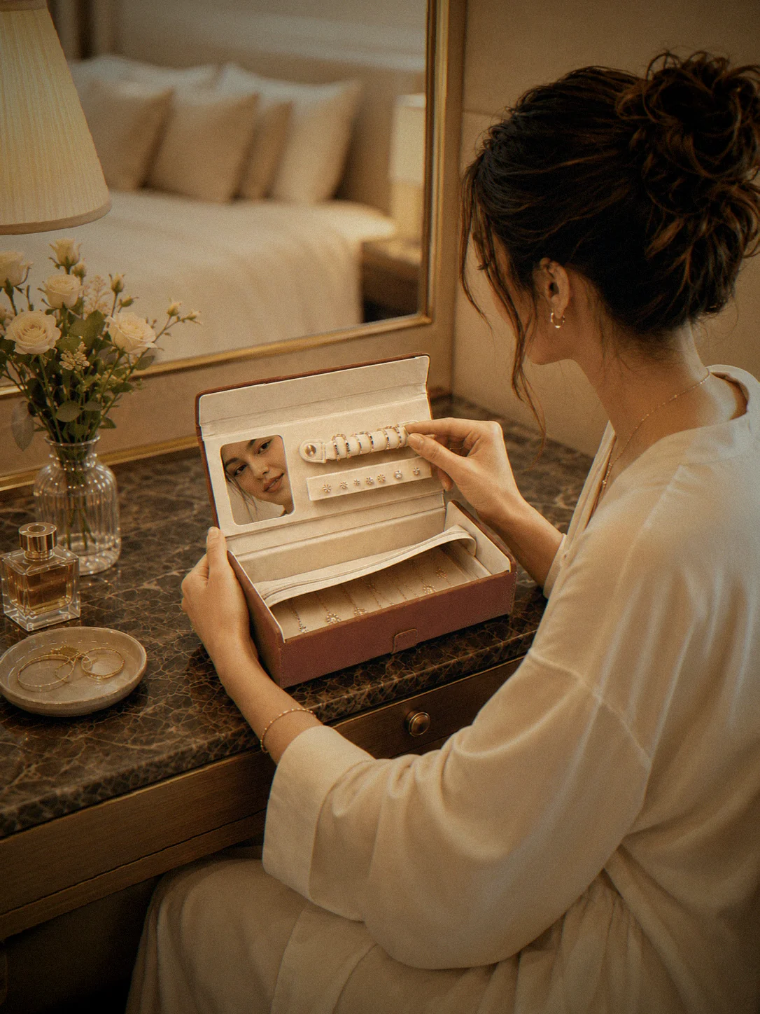 A woman at a hotel vanity taking a ring from the box, her face in the lid mirror